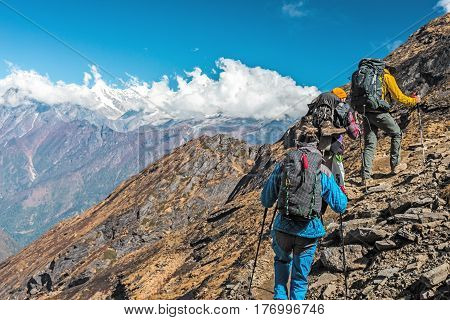 People travelling in Mountains walking up on steep rocky Path back View unrecognisable faces and copy space on left
