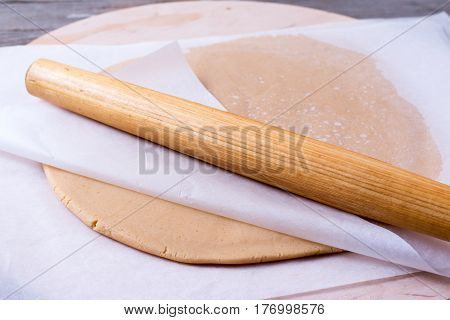 Rolling pin with dough on a wooden background, close up