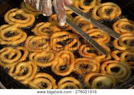 Close Up Of  Golden Color Jalebi Being Soaked In Sugar Syrup By Hand Using A Fork In Daylight In The