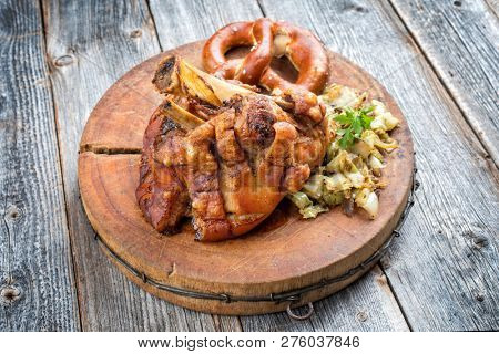 Traditional Bavarian schweinshaxe with coleslaw and preztel as closeup on a wooden cutting board
