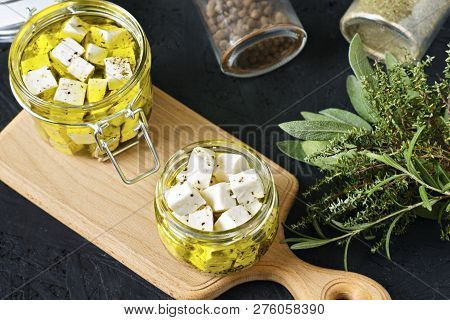 Marinated Feta In A Glass Jar And Spices On A Black Background.