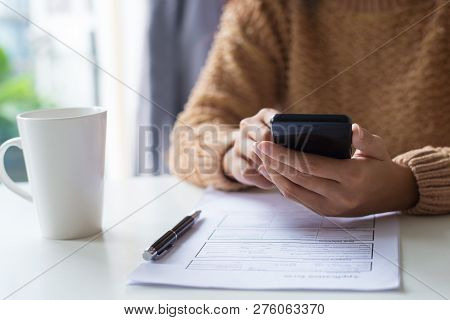 Close-up Of Business Lady Using Gadget While Examining Document. Unrecognizable Woman In Warm Sweate
