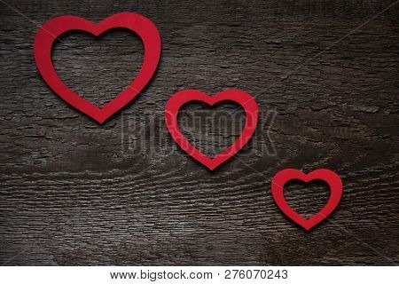 Three Red Hearts Are Located Diagonally On An Old Wooden Brown Wooden Board, One Smaller Than The Ot