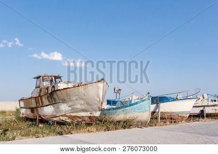 Abandoned Old Rusty Ships And Wooden Boats Staying In Row On The Sea Coast Against Blue Sky With Sma