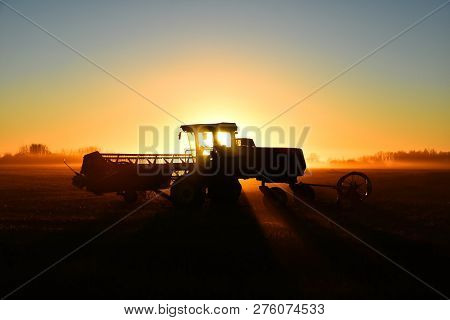 A Silhouette Image Of Agricultural Equipment In A Field At Sunset.