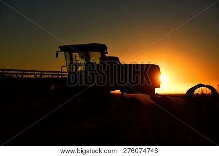 A Silhouette Image Of Agricultural Equipment In A Field At Sunset.