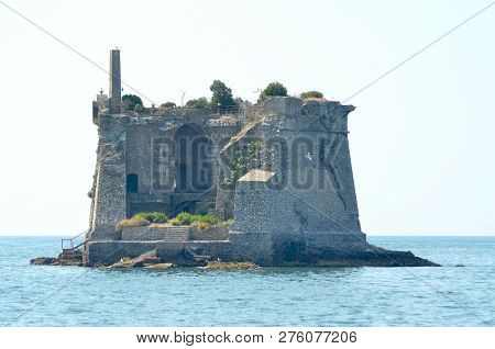 The Remains Of A Stone Tower Cover A Small Rocky Island In A Calm Ocean. Arches And Stairwells Are V
