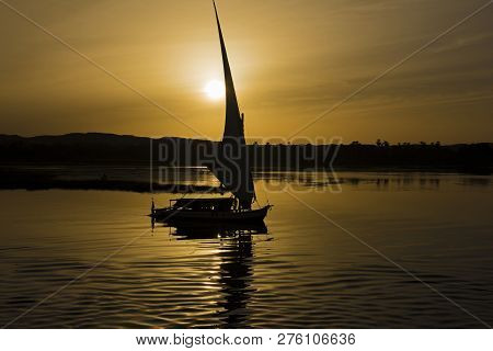 Silhouette Of Traditional Egyptian Felluca Sailing Boat On River Nile With Reflection At Aswan In Ev