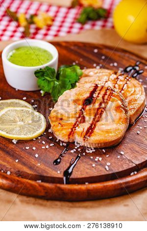 Grilled Fish Steak Served With Sauce And Lemon On Wooden Cutting Board. Close Up
