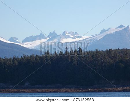 Snowcapped Mountains Tower Over The Tongass National Forest Off The Alaskan Coast.