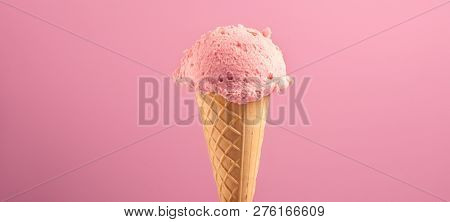 Ice cream cone close-up. Pink Icecream scoop in waffle cone over pink background. Strawberry or raspberry flavor. Sweet dessert closeup, wide angle