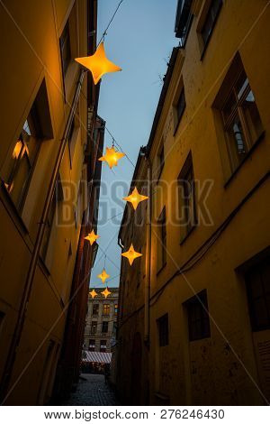 Narrow Rozena Street In Old Town Riga, Latvia With Stars Garland. Christmas Decoration On The Europe