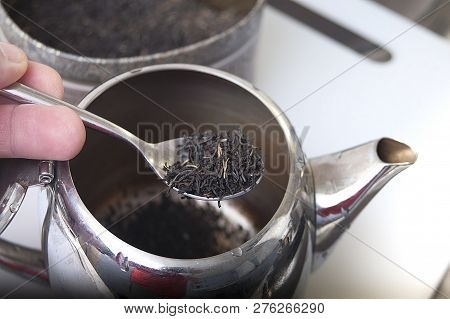 Macro Shot Of A Hand Holding Silver Spoon With Tea Above A Tea Pot