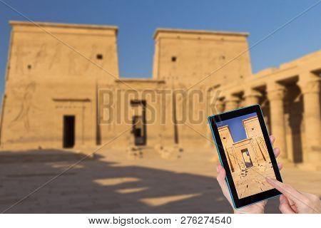 Hands Of Tourist Touching Tablet Screen With A Focused Entrance To The Philae Temple. Intentionally 