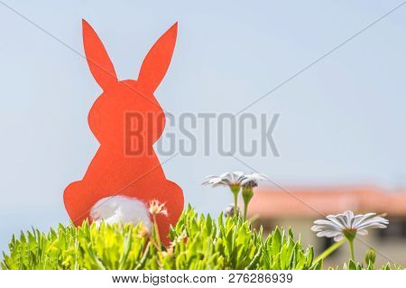 Creative Easter Concept Photo Of Red Paper Rabbit In The Chamomile Flowers And Green Grass On The Bl