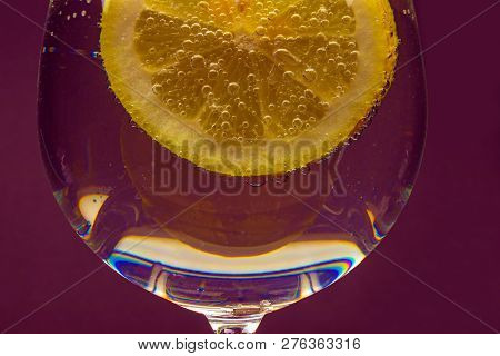 A Glass Of Water With A Slice Of Lemon With Bubbles Isolated On A Purple Background.