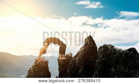 man doing complex Yoga exercise headstand. Amazing Yoga landscape in beautiful mountains. Dangerous stunts traceur standing on his hands on the edge of a cliff.