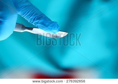 Surgeon Arms In Sterile Uniform Holding Sharp Knife While Operating Patient In Surgical Theatre Clos