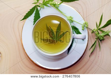 Marijuana Tea. Hemp Tea. Cannabis Tea in a White Tea Cup with a Marijuana Leaf and Stem with Flowers and Leaves on a Wooden Tree Stump serving tray. Room for text. 
