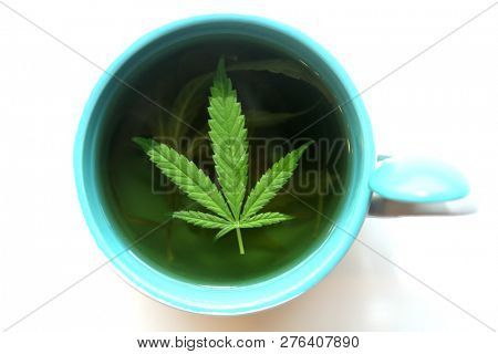 Hemp Tea. Marijuana Tea in a Tea Cup with a Cannabis Leaf and a Stem with Leaves and Flowers. Isolated on white. Room for text. 