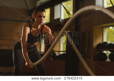 Fit, sporty and athletic sportswoman working in a gym. Woman training using battle ropes. Sports, athletics and fitness concept.