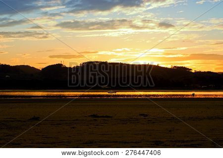 People Silhouettes On The Golden River Background At Sunset Time . Ria De Treto In Laredo, Spain.