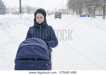 Mother Walks With A Stroller On A Snowy Winter Day