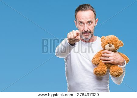 Middle age senior hoary man holding teddy bear over isolated background pointing with finger to the camera and to you, hand sign, positive and confident gesture from the front