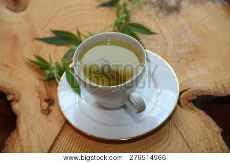 Marijuana Tea. Hemp Tea. Cannabis Tea in a White Tea Cup with a Marijuana Leaf and Stem with Flowers and Leaves on a Wooden Tree Stump serving tray. Room for text. 
