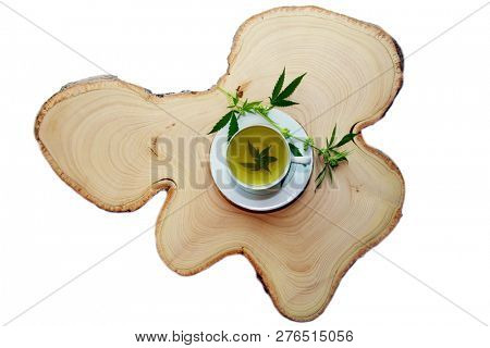 Marijuana Tea. Hemp Tea. Cannabis Tea in a White Tea Cup with a Marijuana Leaf and Stem with Flowers and Leaves on a Wooden Tree Stump serving tray. Room for text. 
