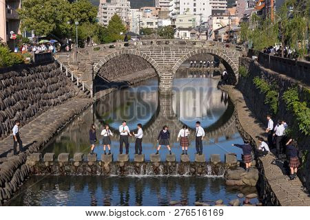 Nagasaki, Japan - October 25, 2018: Students walking on stones in the Nakashima River in front of the Meganebashi