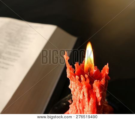 Close-up Of Burning Drippy Rose Colored Candle In Front Of Open Bible