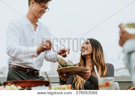 Man serving his friends salad at a rooftop party