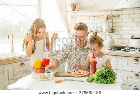 Dad with two small daughters preparing pizza with mushrooms in the kitchen