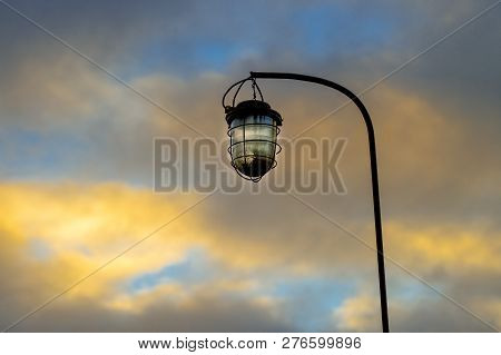 Old Street Lamp On The Background Of A Blocky Sky Suspended On An Iron Rusty Curved Tube