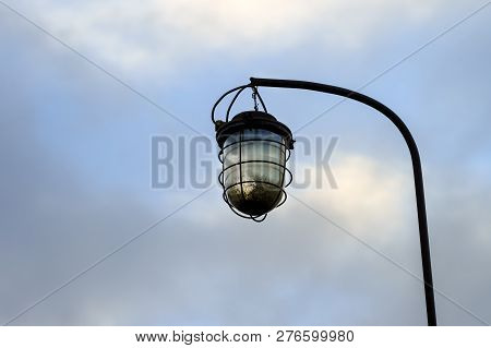 Old Street Lamp On The Background Of A Blocky Sky Suspended On An Iron Rusty Curved Tube