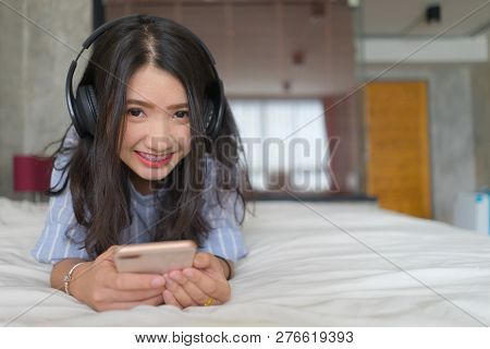 Happy Woman With Headphones Listening Music On Mobile Phone On Bed At Home Smiling With Internet Son