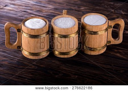 Three Oak Mugs With Beer Inside. On Dark Wooden Background