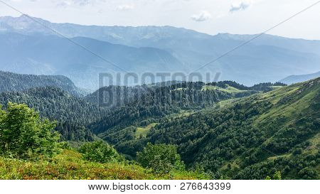 The View From The Height Of A Green Mountain Valley With Residential Buildings Surrounded By High Mo
