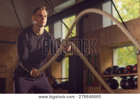 Fit, sporty and athletic sportsman working in a gym. Man training using battle ropes. Sports, athletics and fitness concept.