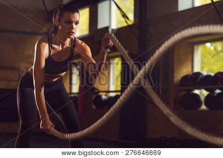 Fit, sporty and athletic sportswoman working in a gym. Woman training using battle ropes. Sports, athletics and fitness concept.