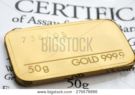 Minted Gold Bar Weighing 50 Grams Fineness 999.9 On The Background Of The Certificate.