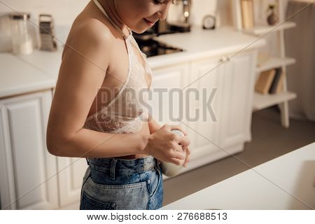 Cropped Shot Of Smiling Girl In Lace Bralette And Jeans Opening Bottle Of Milk At Home