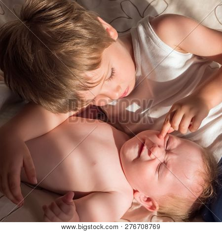 Elder Brother Is Playing With The Newborn. Cute Boy Lovingly Playing With His Baby Sister. The Conce