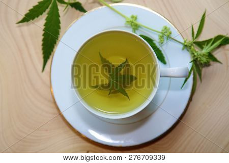 Medical Marijuana Tea. Hemp Tea. Cannabis Tea in a White Tea Cup with a Marijuana Leaf and Stem with Flowers and Leaves on a Wooden Tree Stump serving tray. Room for text. 

