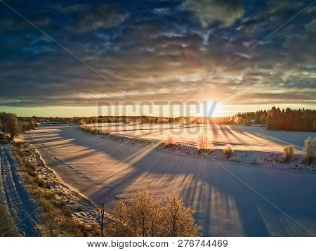 The Sun Rises Over The Frozen River On A Cold Morning In The Rural Finland. Everything Is Covered Wi