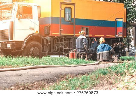 Emergency Repair Service Of The Water Canal. Workers In Helmets Are Sitting Near The Car. Toned