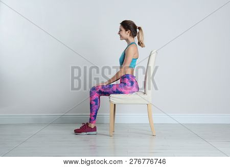 Young Woman Resting In Chair After Sports Training Near White Wall. Home Fitness