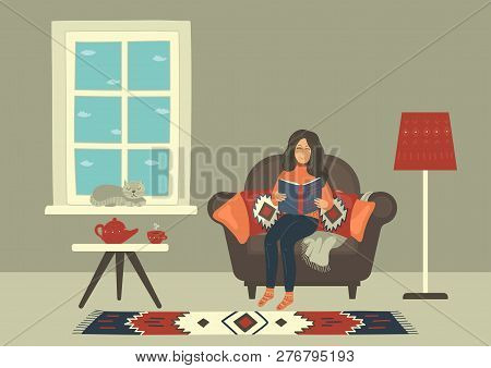 Woman In Cozy Armchair Reading Book And Drinking Hot Tea Near The Window.
