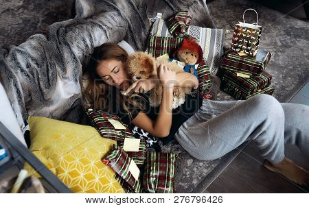 Young Beautiful Lady Playing With Her Small Puppy On A Grey Couch. Cozy Home Atmosphere, A Lot Of So